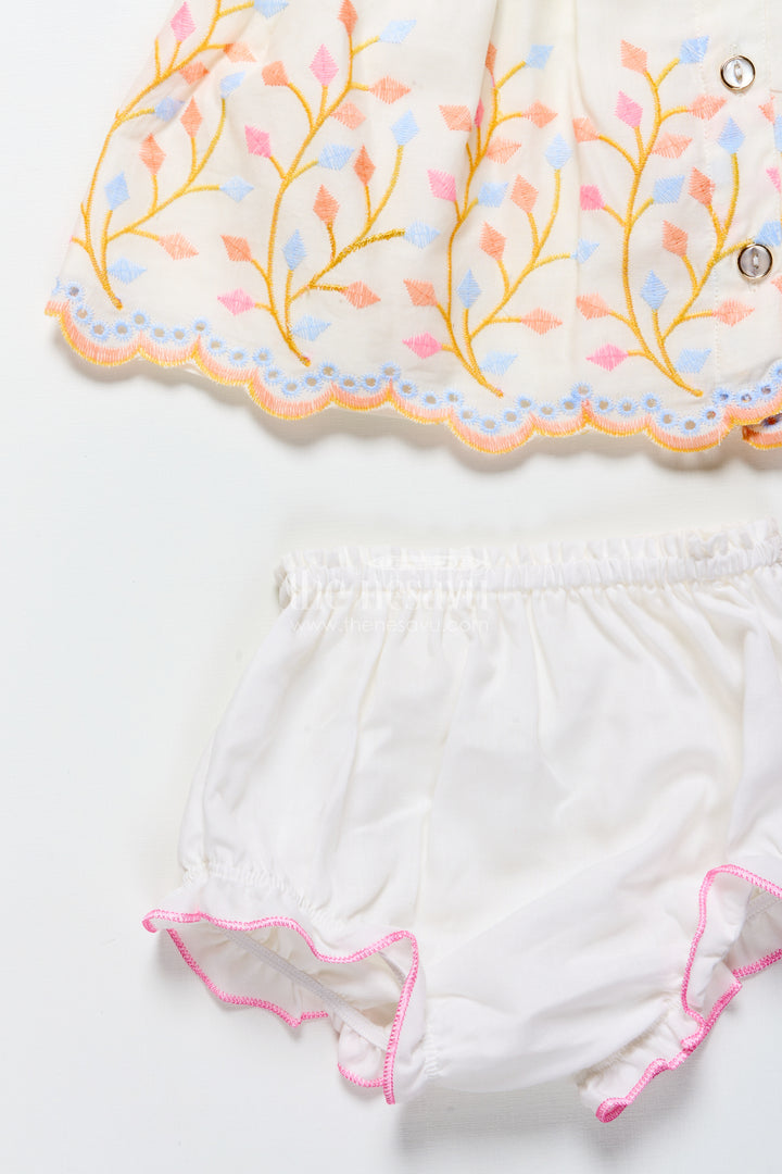 White baby frock with pastel floral embroidery and ruffled hem